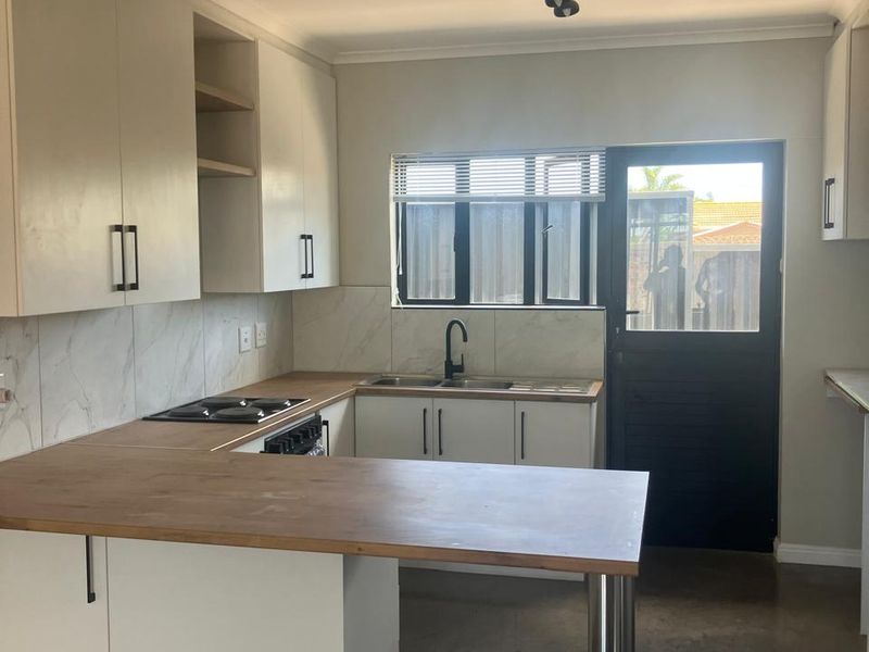 A modern, clean kitchen featuring white cabinetry, wooden countertops, a built-in hob, and a double sink with direct access to the exterior.