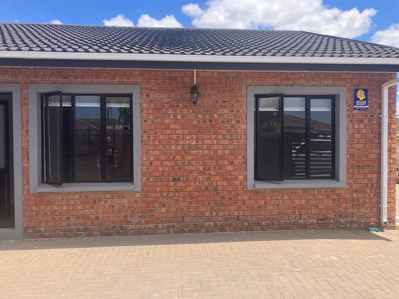 A well-maintained face brick exterior facade featuring modern dark aluminium window frames and a paved driveway area.