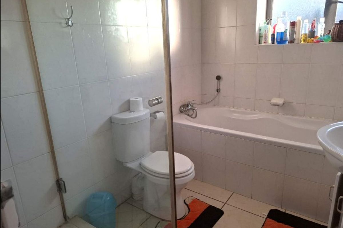 A functional bathroom featuring a built-in bathtub, shower screen, toilet, and basin with tiled walls and flooring.