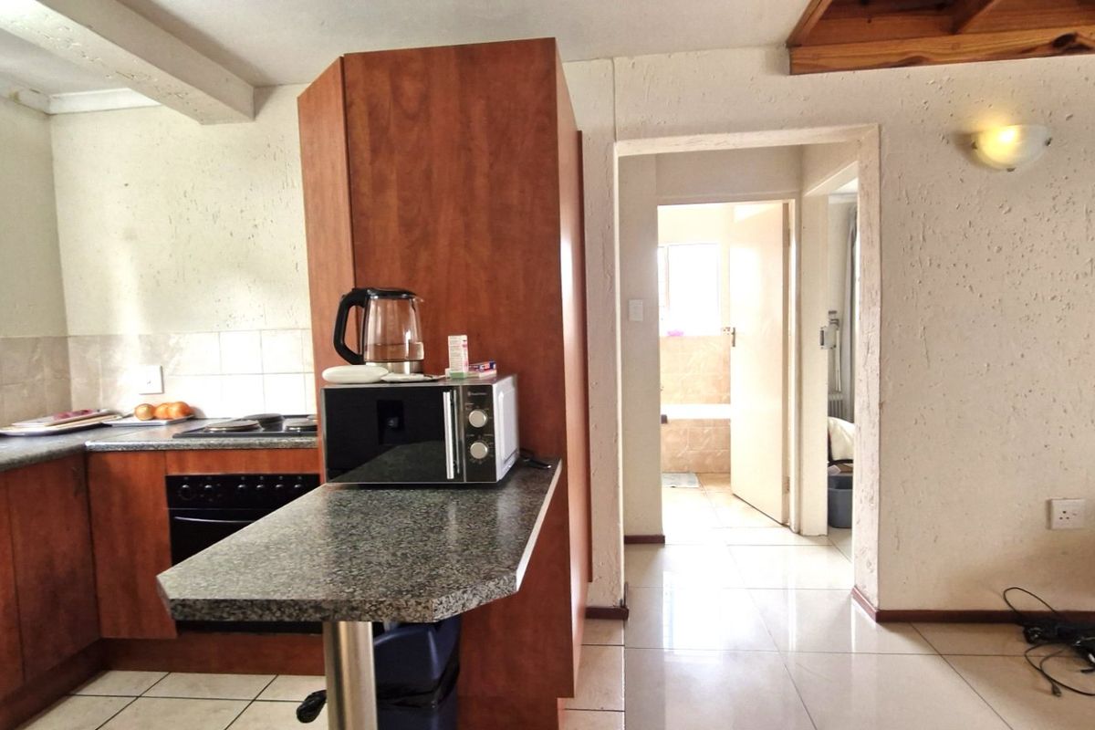 A functional kitchen featuring wood-finish cabinetry, laminate countertops, and built-in appliances, with tiled flooring and direct access to the hallway and bathroom.