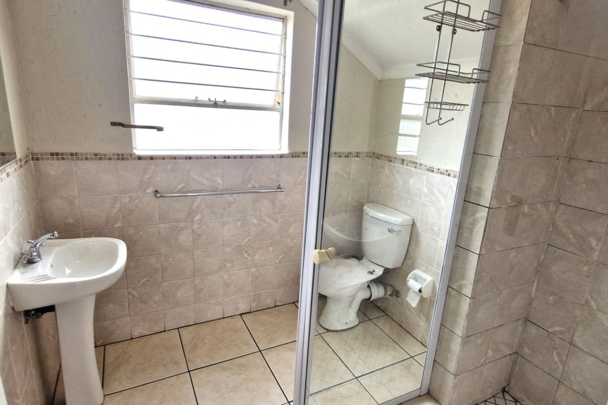 A functional bathroom featuring a pedestal basin, toilet, and a glass-enclosed shower with neutral tiled walls and flooring.