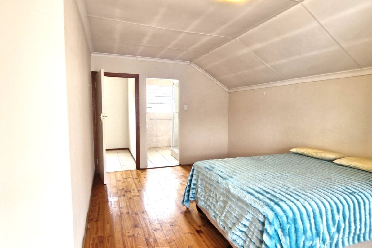 A bedroom featuring timber flooring and a sloped ceiling, with direct access to an adjoining bathroom area.