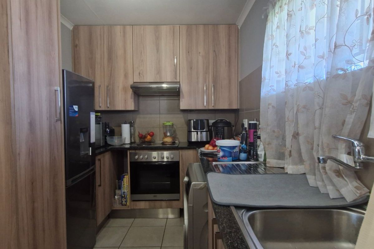 A functional kitchen featuring wood-look laminate cabinetry, built-in oven with extractor fan, tiled splashbacks, and a stainless steel sink.
