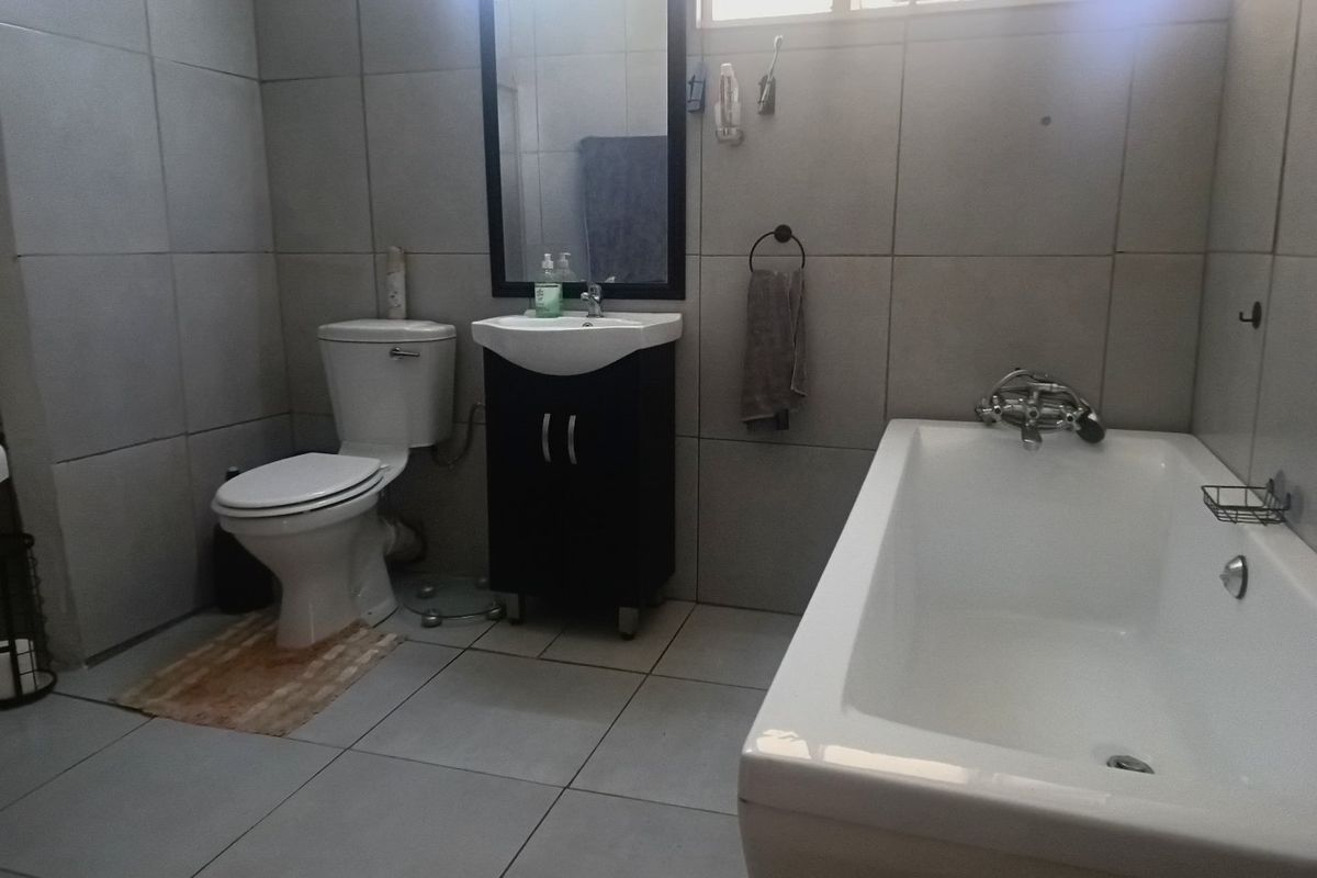 A functional bathroom featuring a bathtub, a vanity cabinet with a washbasin, and full-height wall tiling.