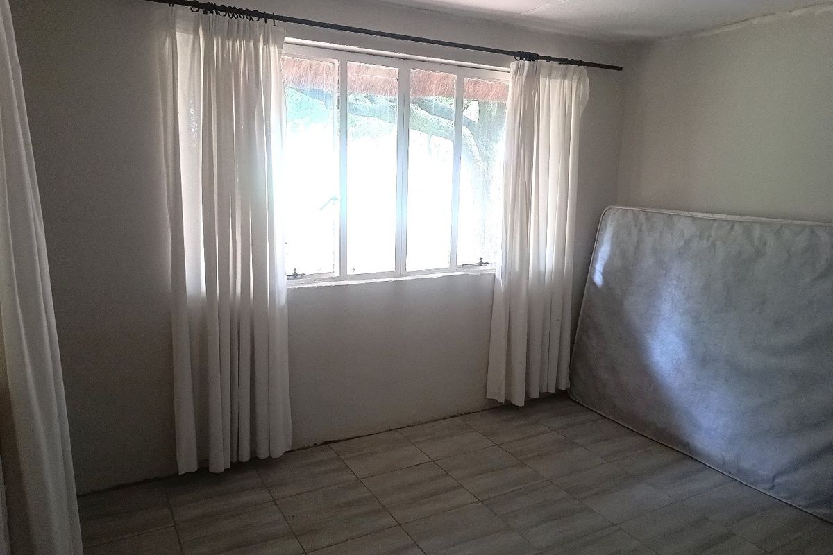A vacant bedroom featuring tiled flooring and a large window with curtain rod, offering a blank canvas for potential interior design updates.