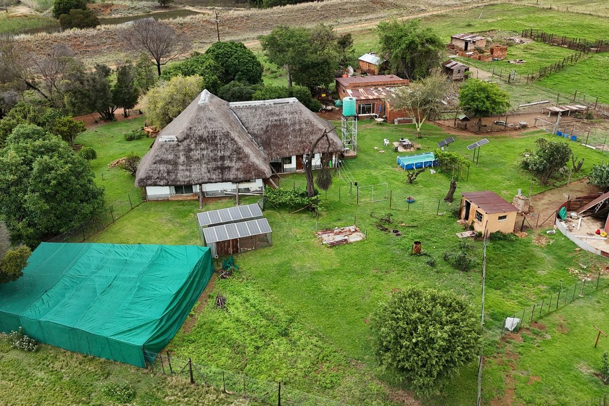 Aerial view of a farm property featuring a main thatched-roof dwelling, multiple outbuildings, solar infrastructure, and surrounding agricultural land.