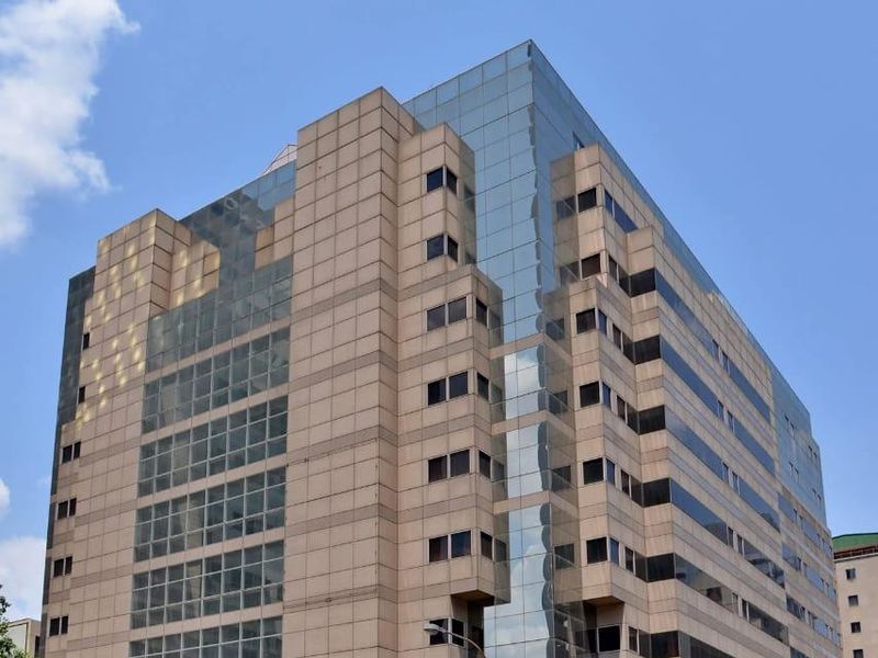 A multi-story commercial apartment building featuring a modern glass and panel facade, situated on a busy urban street corner.