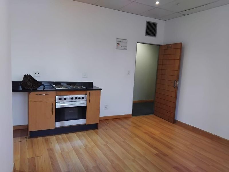 A compact kitchen area featuring a built-in oven, hob, and black granite countertop, set against a backdrop of laminate flooring and a wooden door.