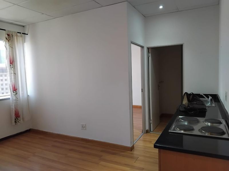 Open plan living area featuring laminate flooring, a drop ceiling, and a compact kitchen corner with a built-in electric hob and granite countertop.