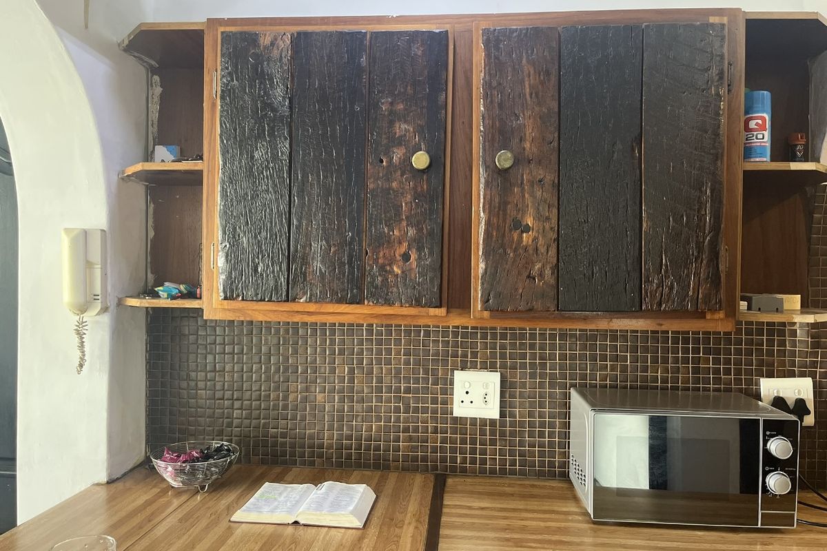 A kitchen area featuring rustic wooden cabinetry, a dark mosaic tile backsplash, and laminate countertops, showing signs of wear and dated finishes.