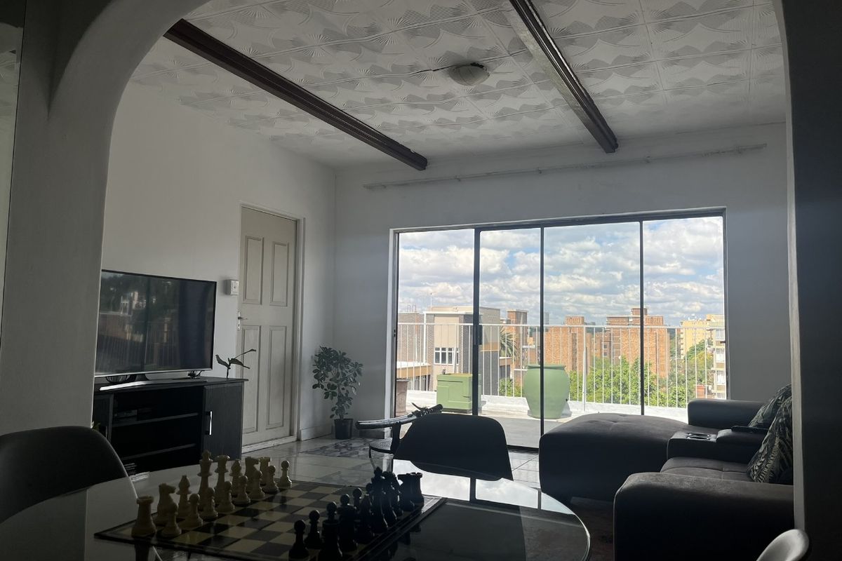 Spacious living area featuring an arched entryway, textured ceiling with exposed beams, and large sliding glass doors leading to an outdoor balcony.