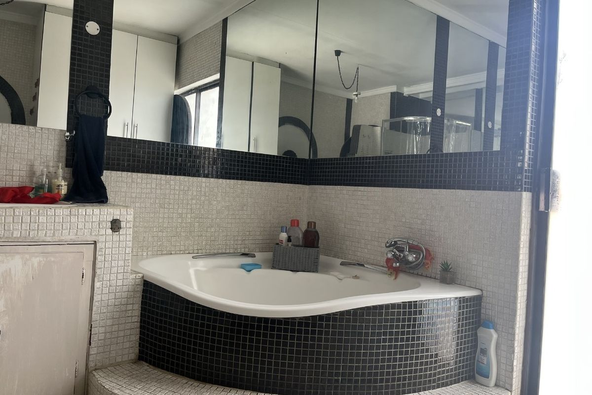 Bathroom featuring a corner bathtub with black and white mosaic tile surround, built-in vanity cabinetry, and a large wall-mounted mirror.