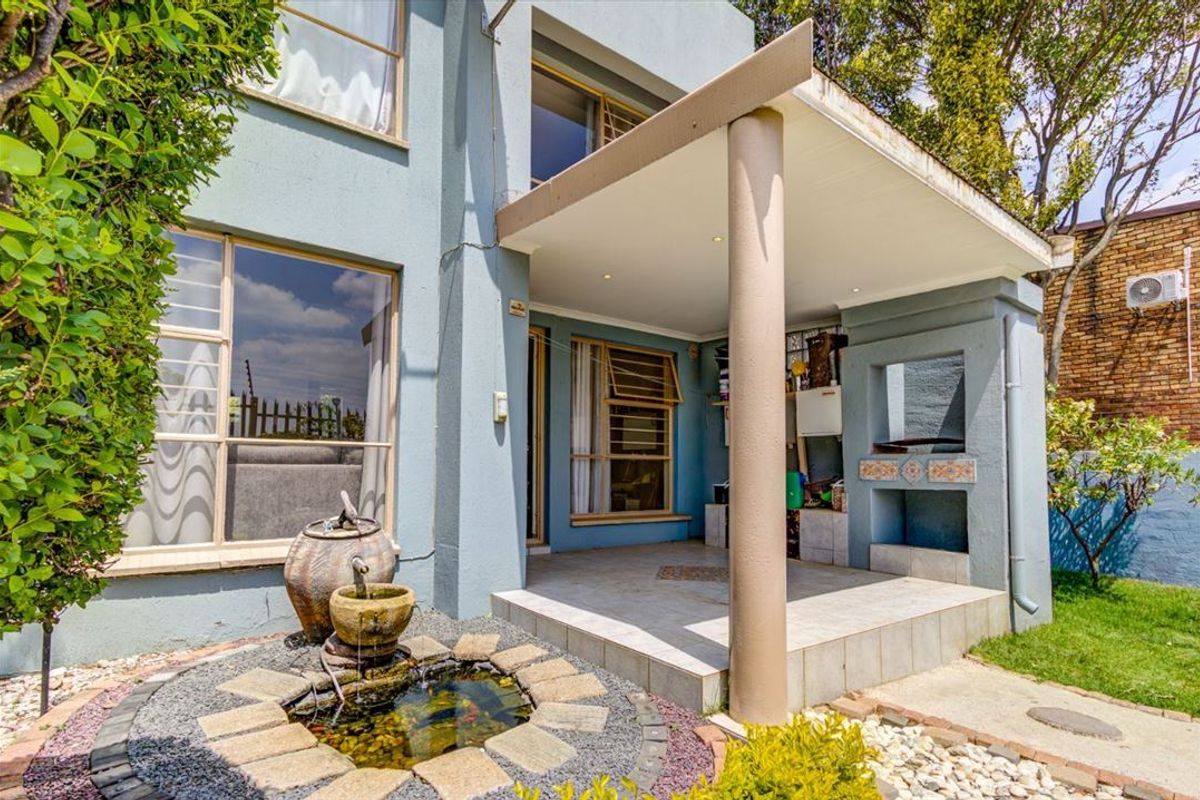 A covered patio area featuring a built-in braai, tiled flooring, and recessed lighting, overlooking a landscaped garden with a stone water feature.