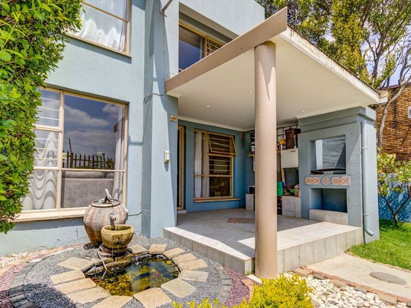 A covered patio area featuring a built-in braai, tiled flooring, and recessed lighting, overlooking a landscaped garden with a stone water feature.