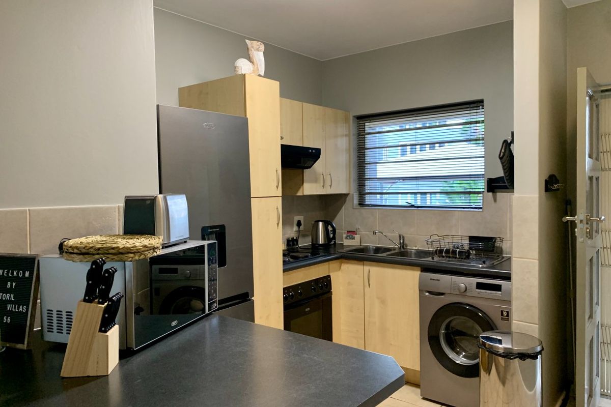 Compact kitchen featuring light wood-finish cabinetry, dark countertops, built-in oven with extractor, and integrated space for laundry appliances.