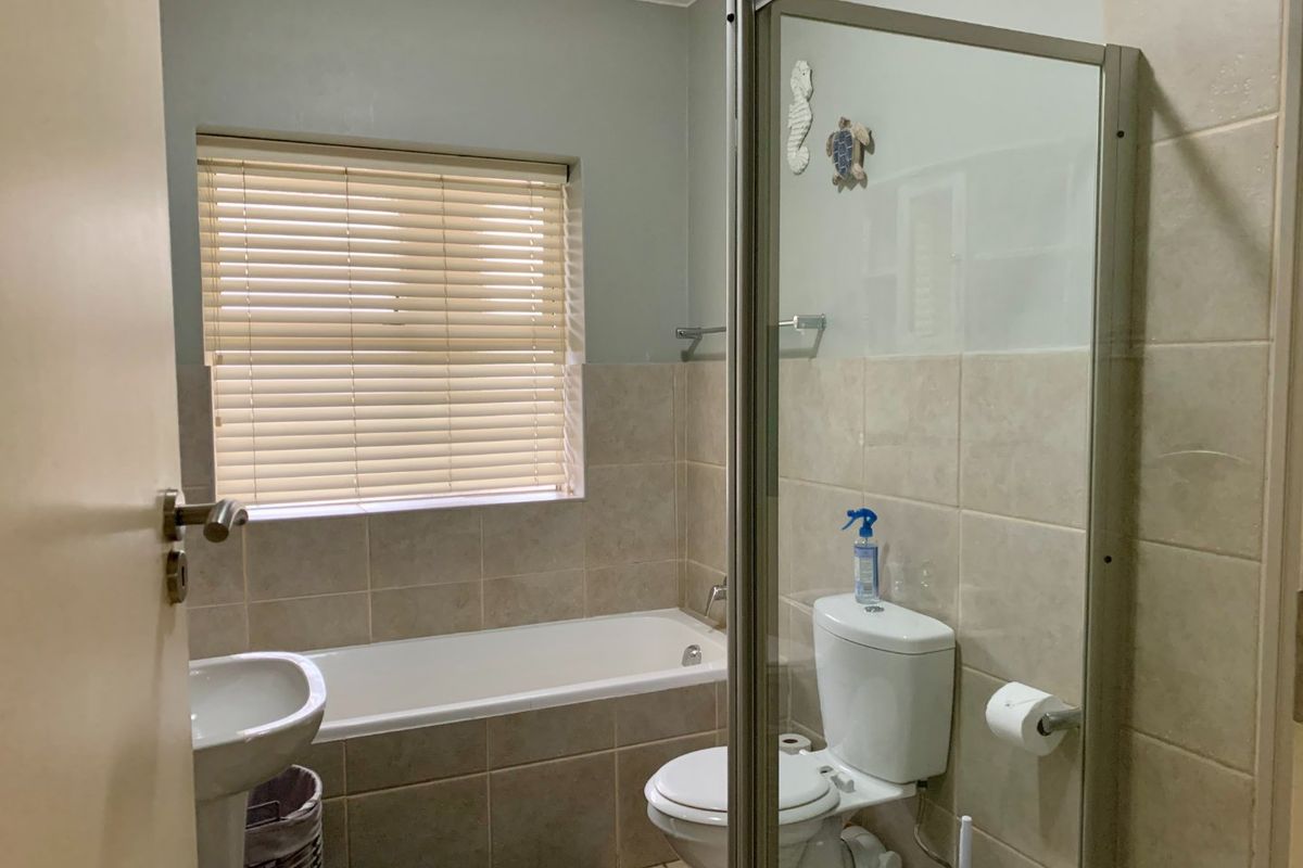 A functional bathroom featuring a pedestal basin, built-in bathtub, separate shower enclosure, and neutral wall tiling with natural light from a window.