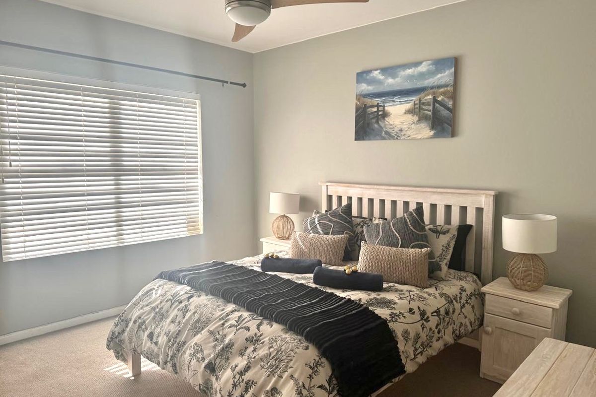 A well-maintained bedroom featuring neutral wall tones, carpeted flooring, a ceiling fan, and venetian blinds for adjustable natural light.