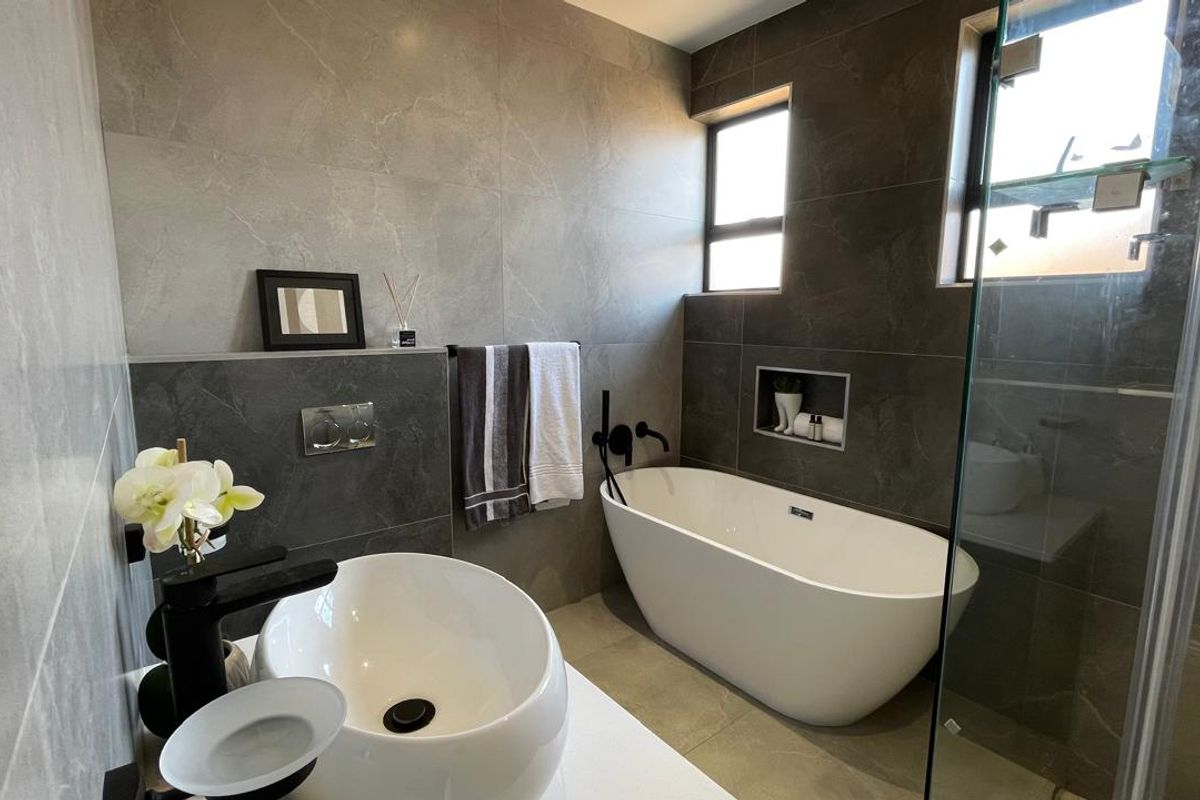 Modern bathroom featuring a sleek freestanding bathtub, vessel sink with matte black fixtures, and contemporary large-format grey porcelain wall tiles.