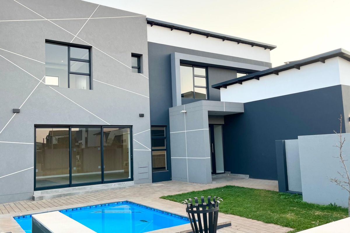 Modern double-story rear elevation featuring a swimming pool, paved patio area, and contemporary architectural design with large sliding glass doors.
