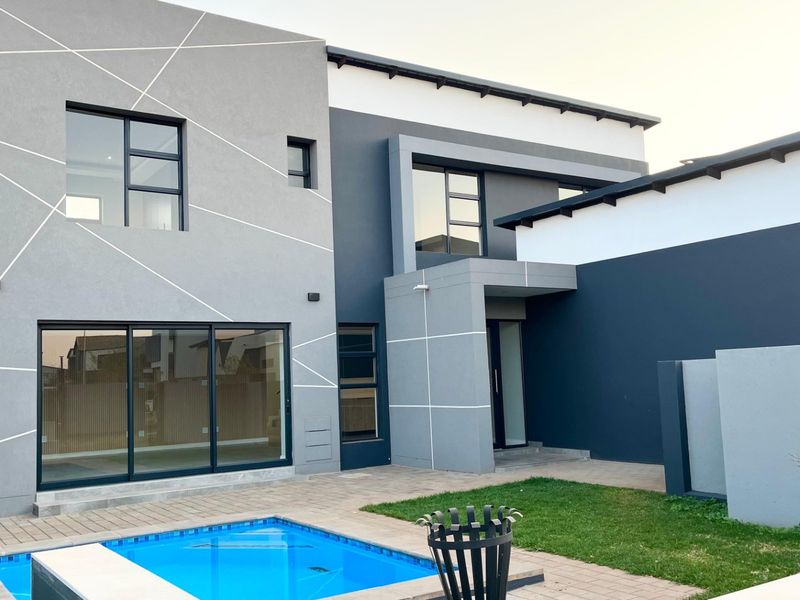 Modern double-story rear elevation featuring a swimming pool, paved patio area, and contemporary architectural design with large sliding glass doors.
