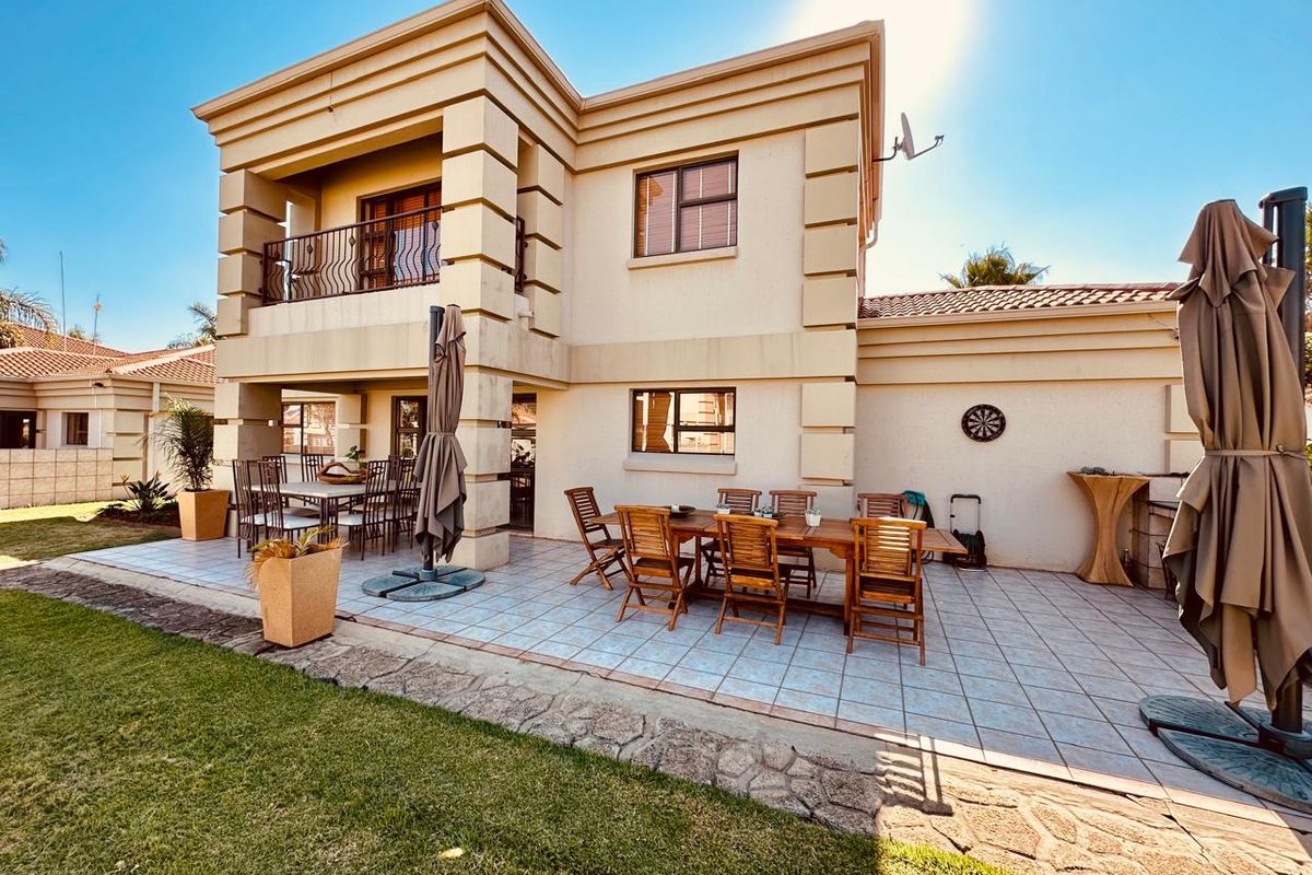 Rear view of a two-story house featuring a spacious tiled patio, a covered balcony with wrought iron railings, and a well-maintained garden area.