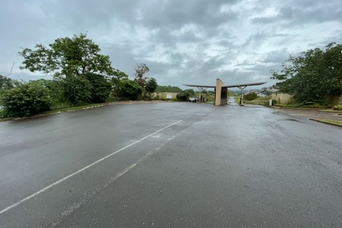 View of the residential estate entrance gate and security access point with paved driveway and surrounding landscaped greenery.