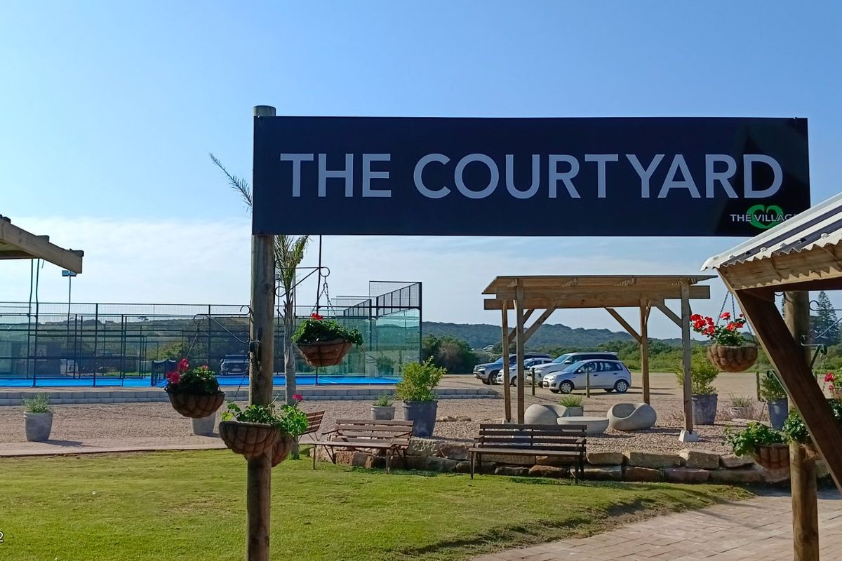 Outdoor recreational area featuring a padel court, landscaped grounds, and a prominent signage structure for The Courtyard.