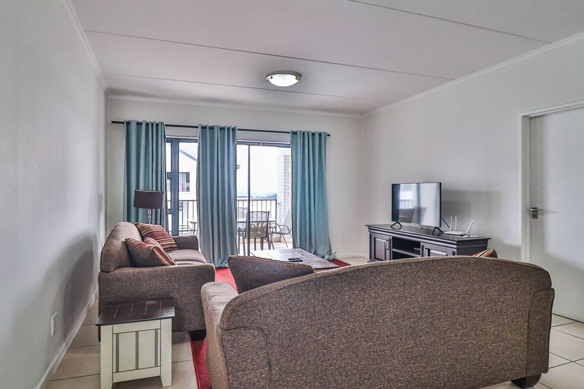 A well-lit living room featuring neutral tiled flooring and a sliding glass door providing access to an outdoor balcony area.