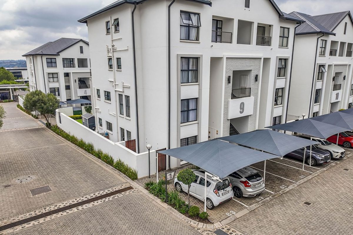 Aerial view of a modern apartment complex featuring paved parking areas with shade sail carports and well-maintained building exteriors.