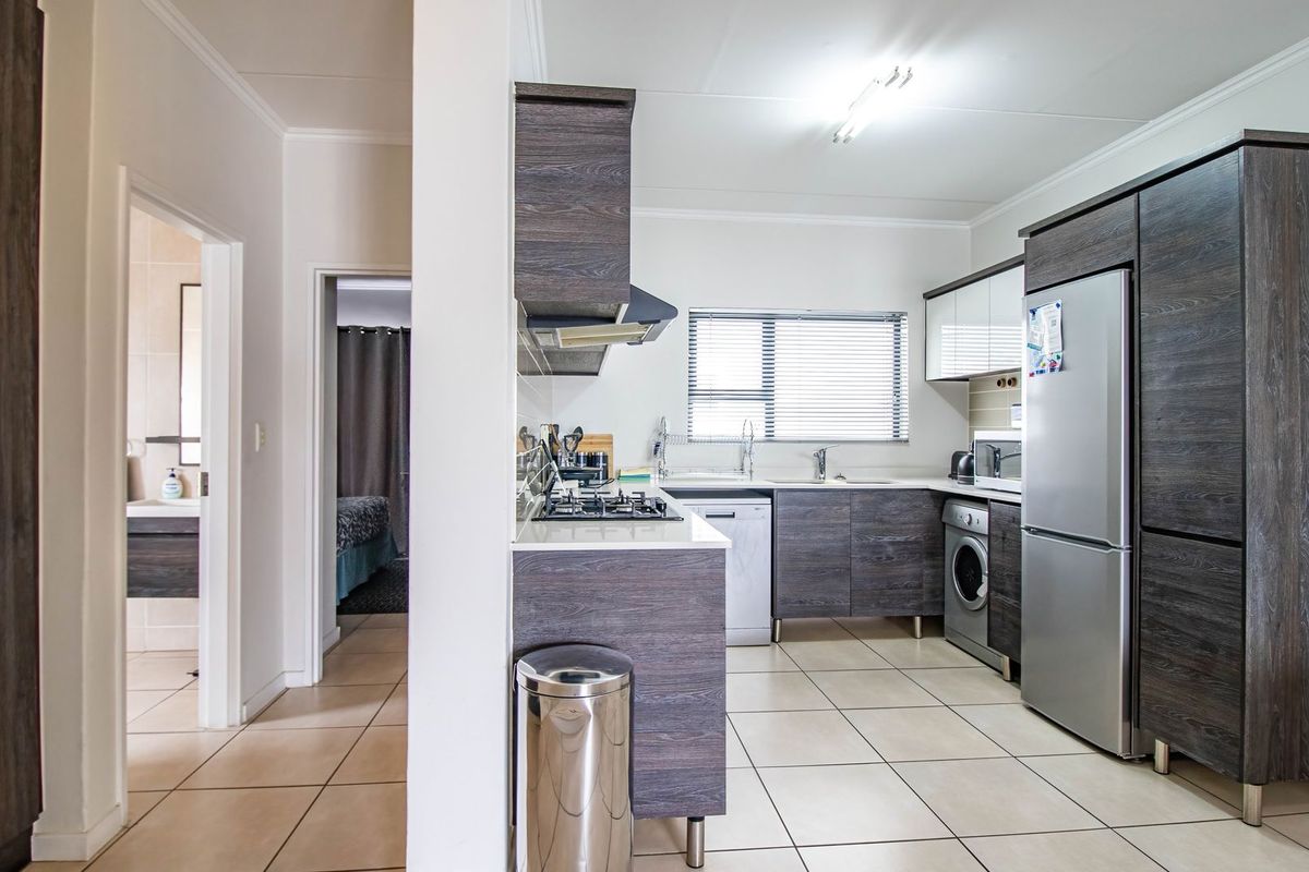 Modern kitchen featuring dark wood cabinetry, gas hob, extractor fan, and tiled flooring, with an open-plan layout leading to adjacent rooms.