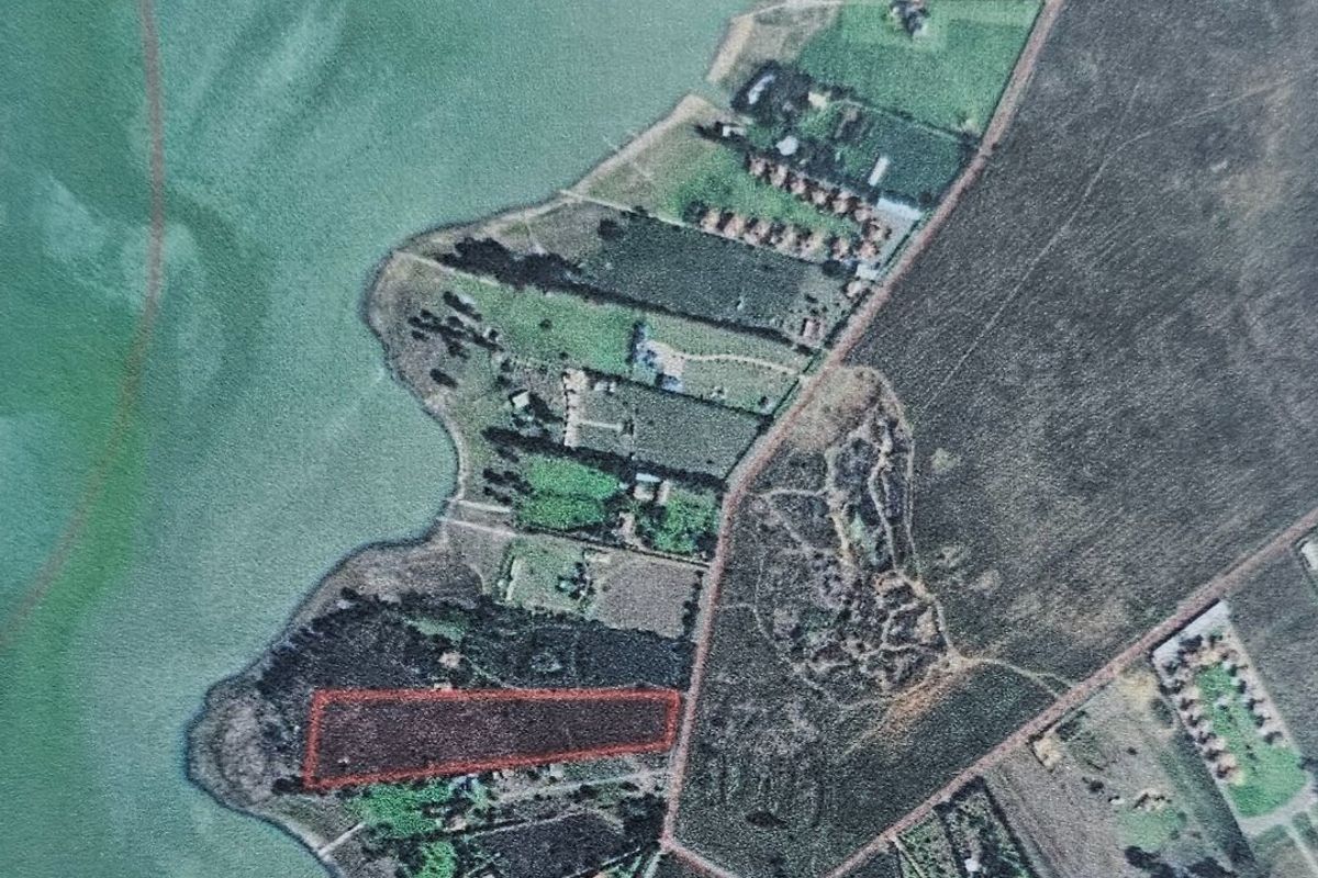 An aerial view showing the vacant land parcel highlighted in red, featuring direct waterfront access and surrounding landscape.