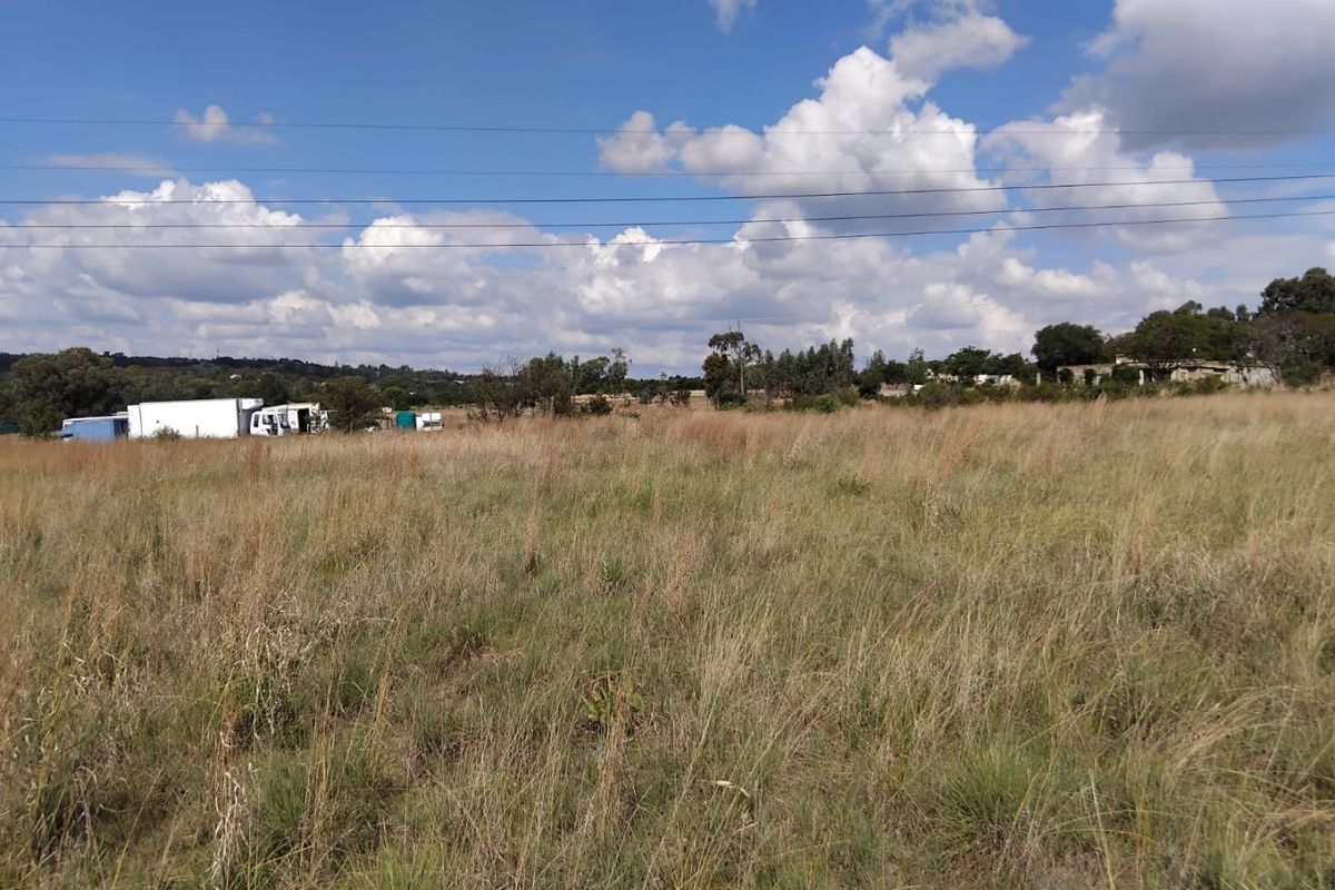 A wide-angle view of a vacant residential plot featuring natural grassland and overhead power lines under a clear blue sky.