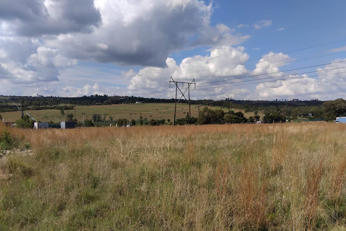A wide-angle view of a vacant residential plot featuring natural grassland and overhead utility infrastructure under a clear sky.