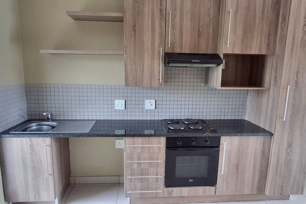 A compact, functional kitchen featuring wood-look laminate cabinetry, granite countertops, a built-in oven with hob, and a tiled backsplash.