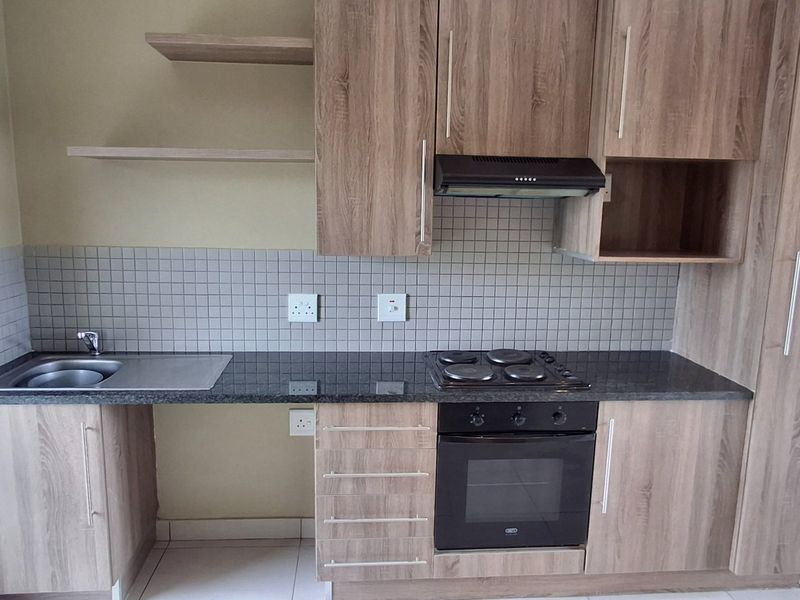 A compact, functional kitchen featuring wood-look laminate cabinetry, granite countertops, a built-in oven with hob, and a tiled backsplash.