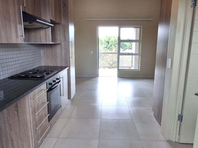 Open plan kitchen and living area featuring modern wood-finish cabinetry, granite countertops, built-in appliances, and tiled flooring leading to a balcony.