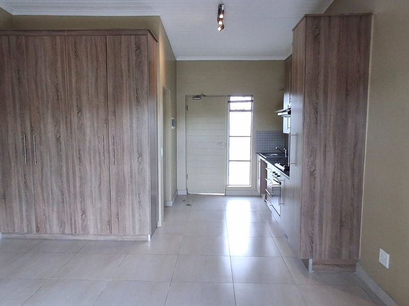 Open-plan living area featuring built-in storage cupboards and a compact kitchen with integrated oven, hob, and extractor fan.