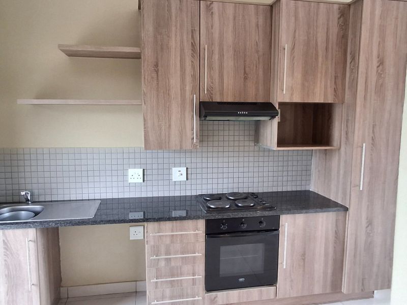 A modern, compact kitchen featuring wood-look laminate cabinetry, granite countertops, a built-in oven with hob, and a tiled splashback.