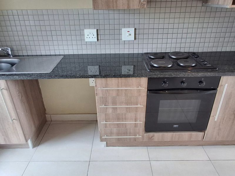 A clean, modern kitchen featuring granite countertops, built-in oven, electric hob, and neutral cabinetry with a tiled backsplash.
