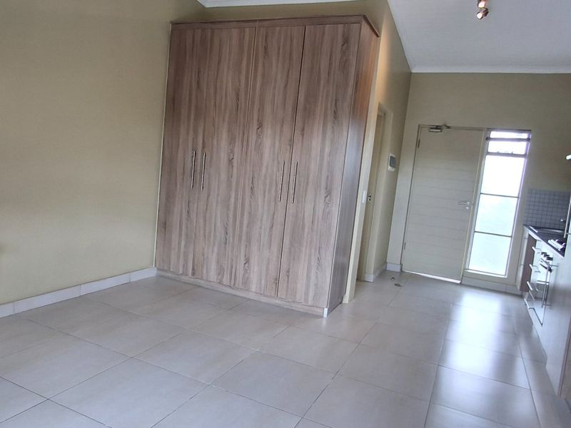 An open-plan living and kitchen area featuring neutral tiled flooring, extensive built-in cabinetry, a built-in desk, and direct access to an exterior door.