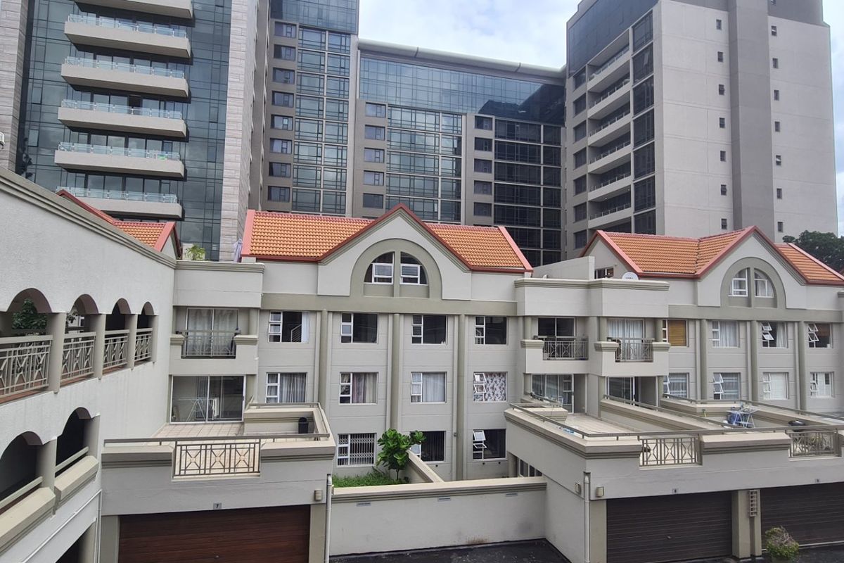 A view of the rear elevation of a multi-story apartment complex featuring terracotta roof tiles, balconies, and integrated garage access.