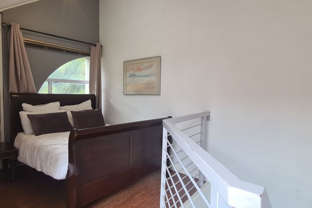A loft-style bedroom featuring laminate flooring, built-in shelving, and a protective railing overlooking the lower level.
