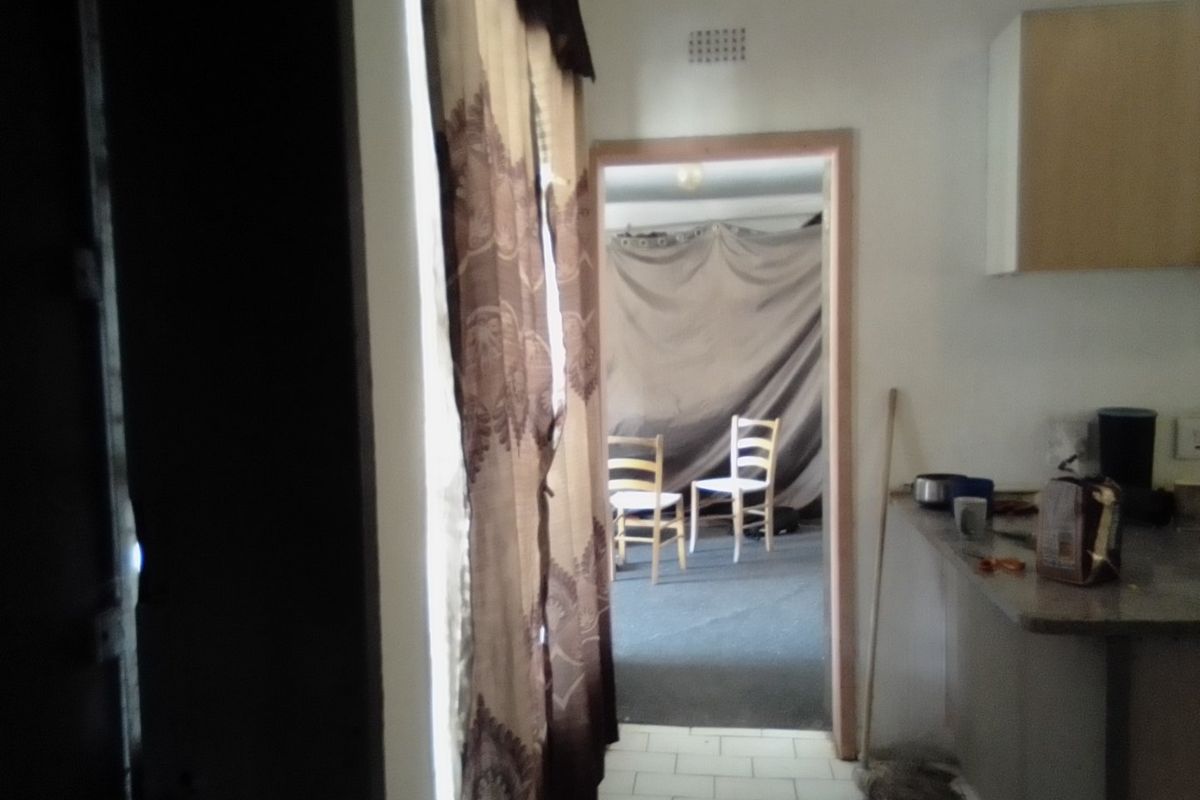 A view from a kitchen area looking into an adjacent room, featuring basic cabinetry, countertops, and tiled flooring in need of modernization.