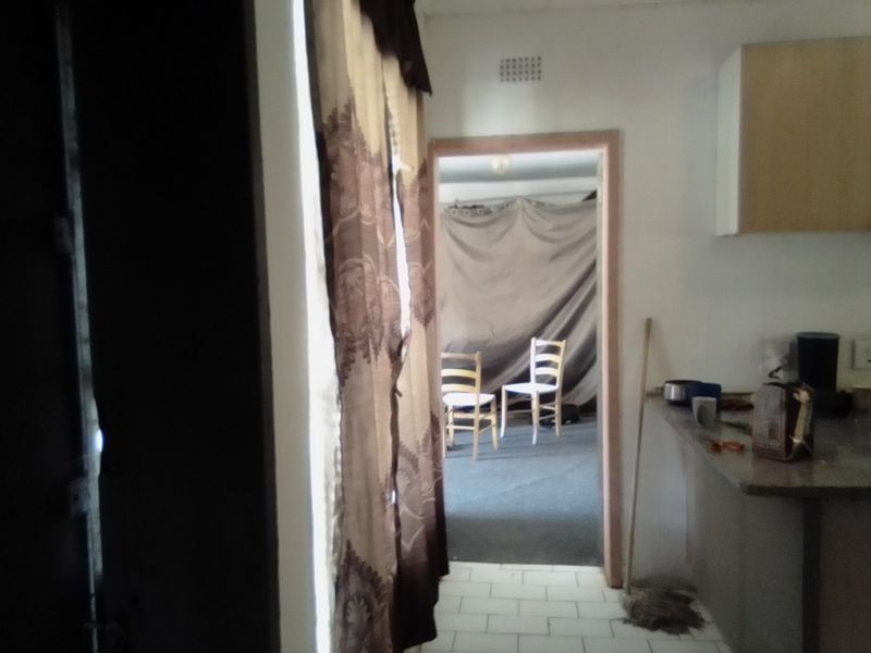 A view from a kitchen area looking into an adjacent room, featuring basic cabinetry, countertops, and tiled flooring in need of modernization.
