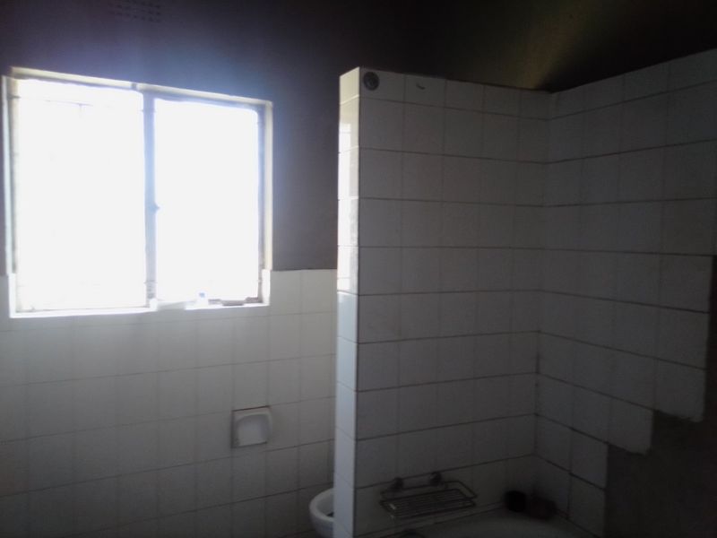 A bathroom space featuring a tiled shower partition, wall-mounted fixtures, and a window, currently requiring completion of wall tiling and general renovation.