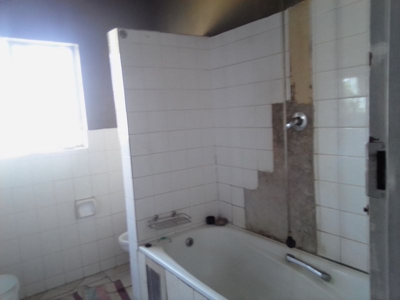 A bathroom featuring a bathtub and shower area with visible damage to the wall tiling and surface, requiring repair and renovation.
