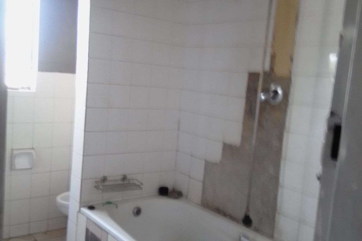 A bathroom featuring a bathtub and toilet, currently requiring repairs to the wall tiling and finishes.