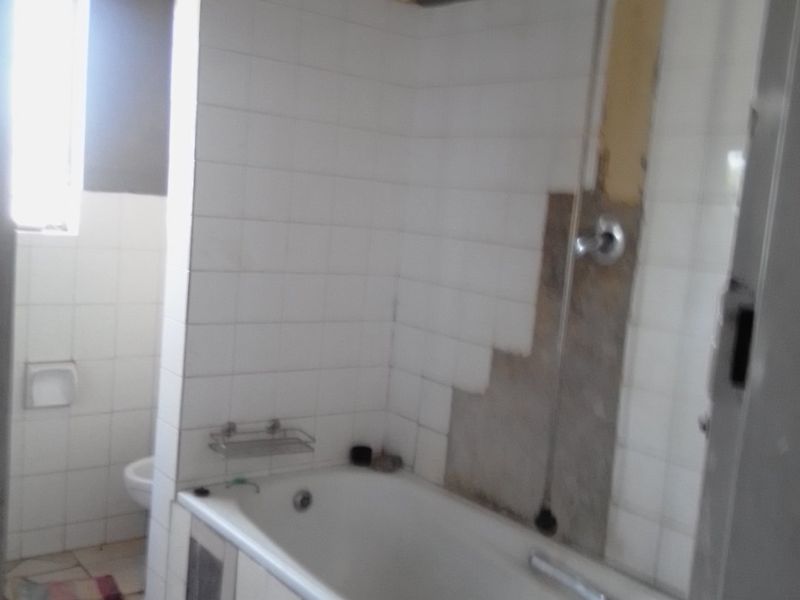 A bathroom featuring a bathtub and toilet, currently requiring repairs to the wall tiling and finishes.