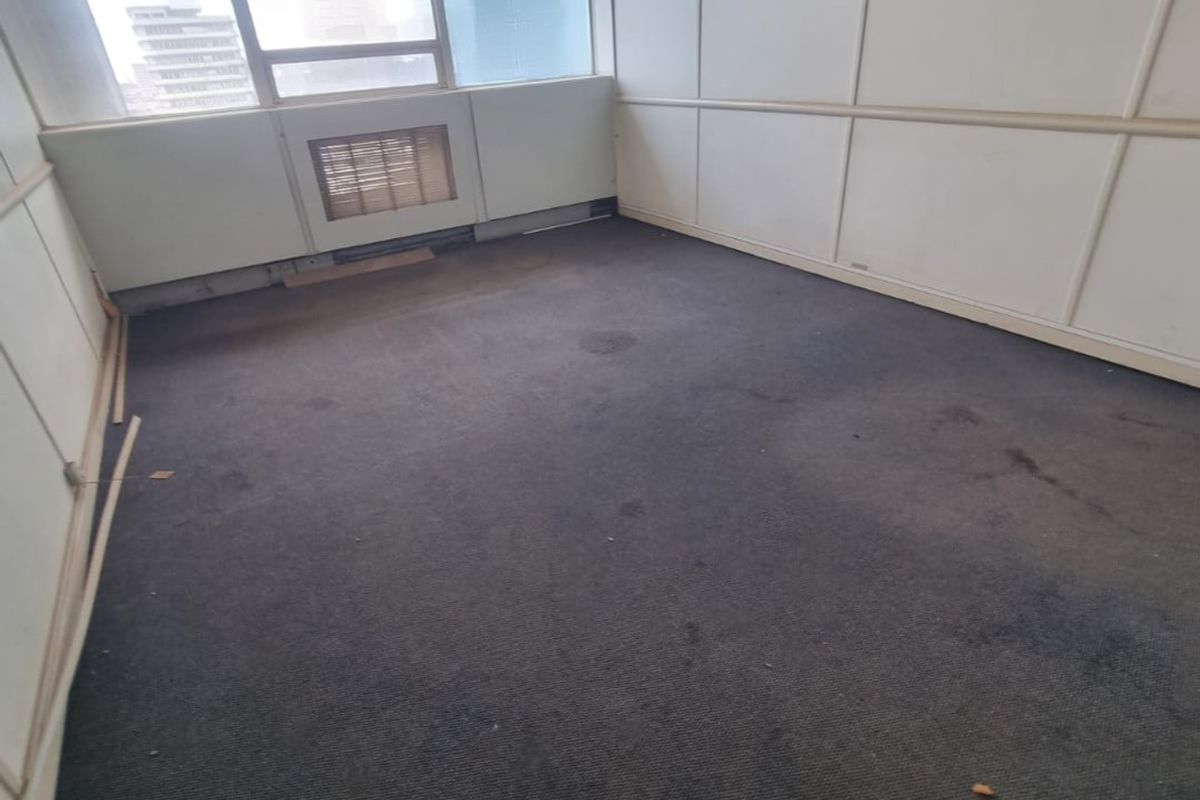 An empty office space featuring partitioned wall panels, carpet flooring, and a built-in HVAC unit, requiring cosmetic updates to improve its professional appeal.