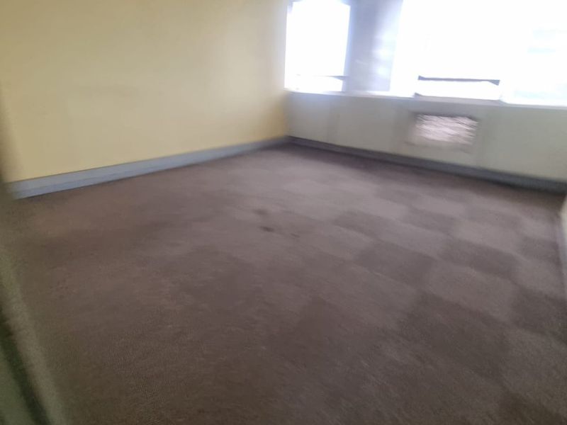 An empty commercial office space featuring carpeted flooring, large windows for natural light, and recessed ceiling lighting.